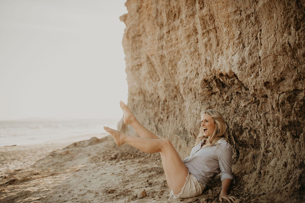 Kali May laughing beside a sunlit coastal cliff