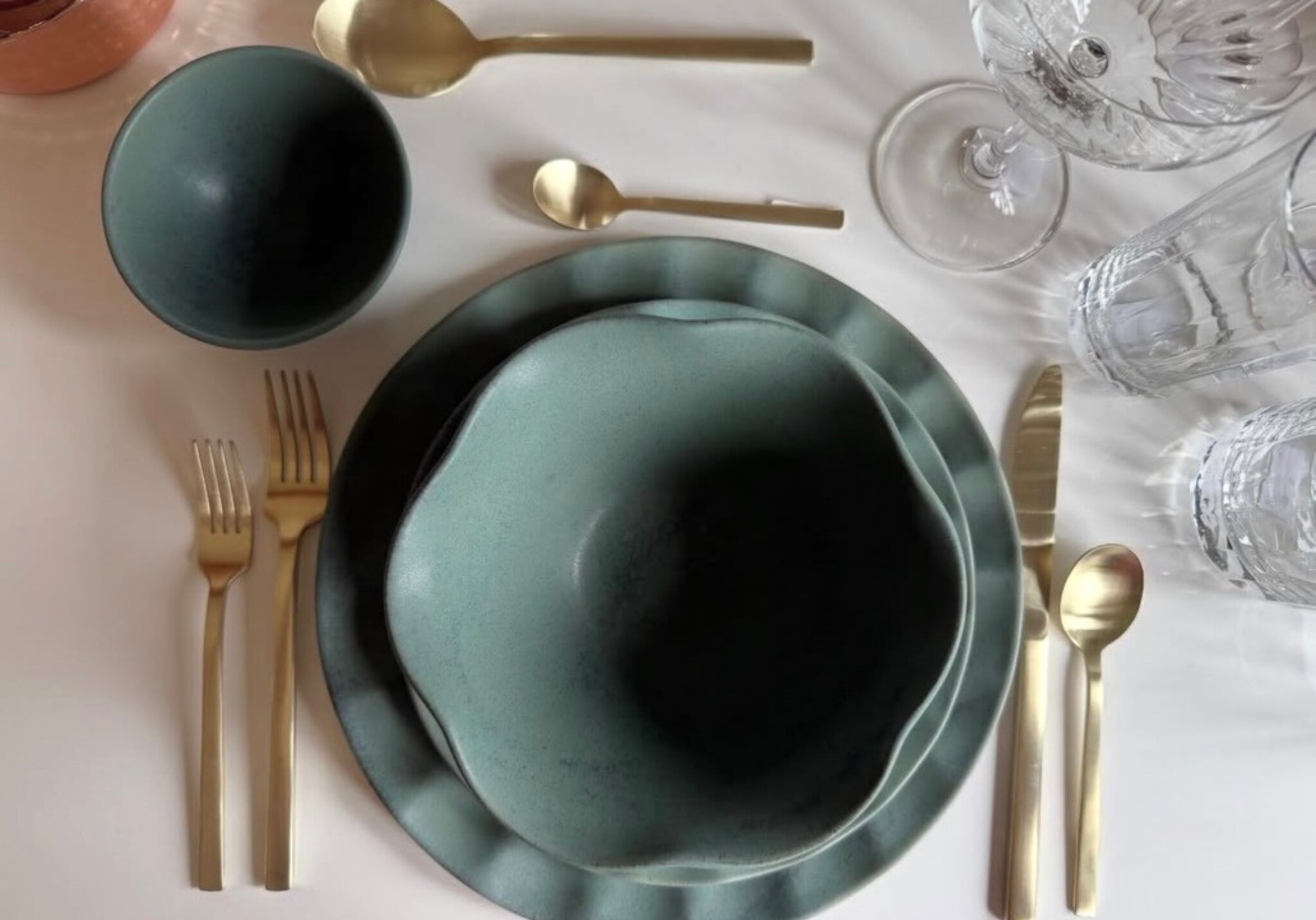 Deep forest-green Matilija Collection dinnerware styled with gold flatware and crystal glassware